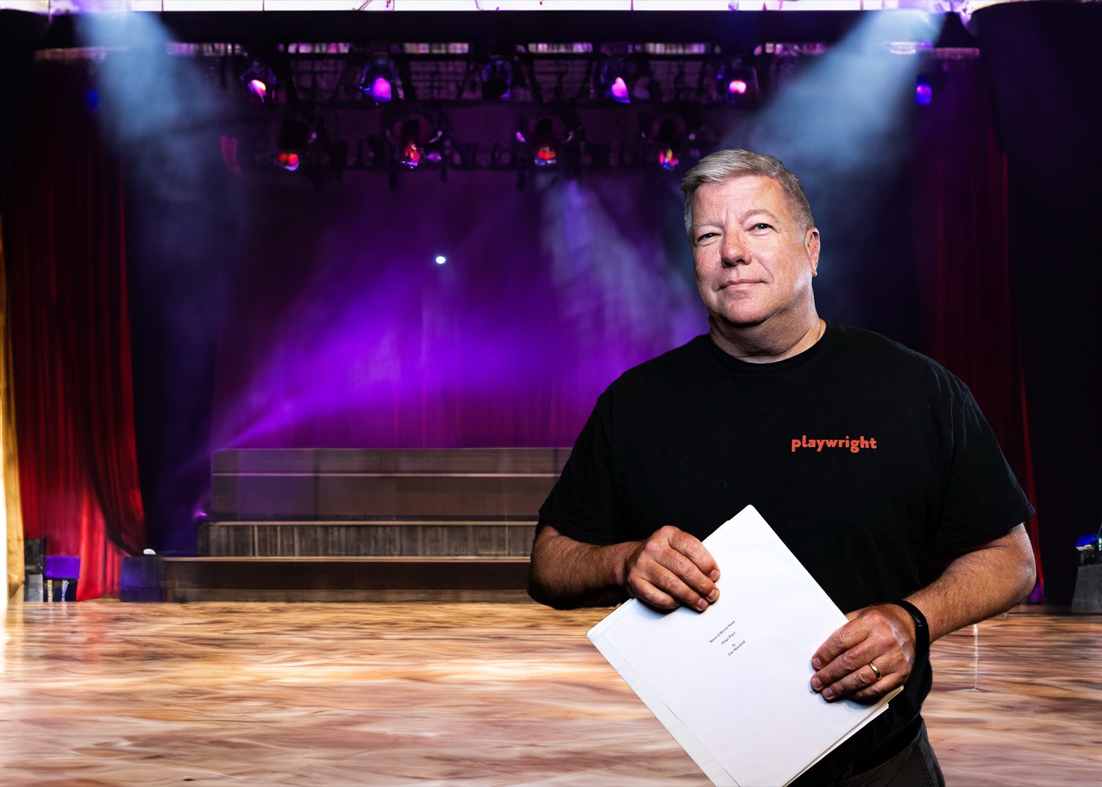 Eric Mansfield standing on a darkened theatre stage, lit from above.